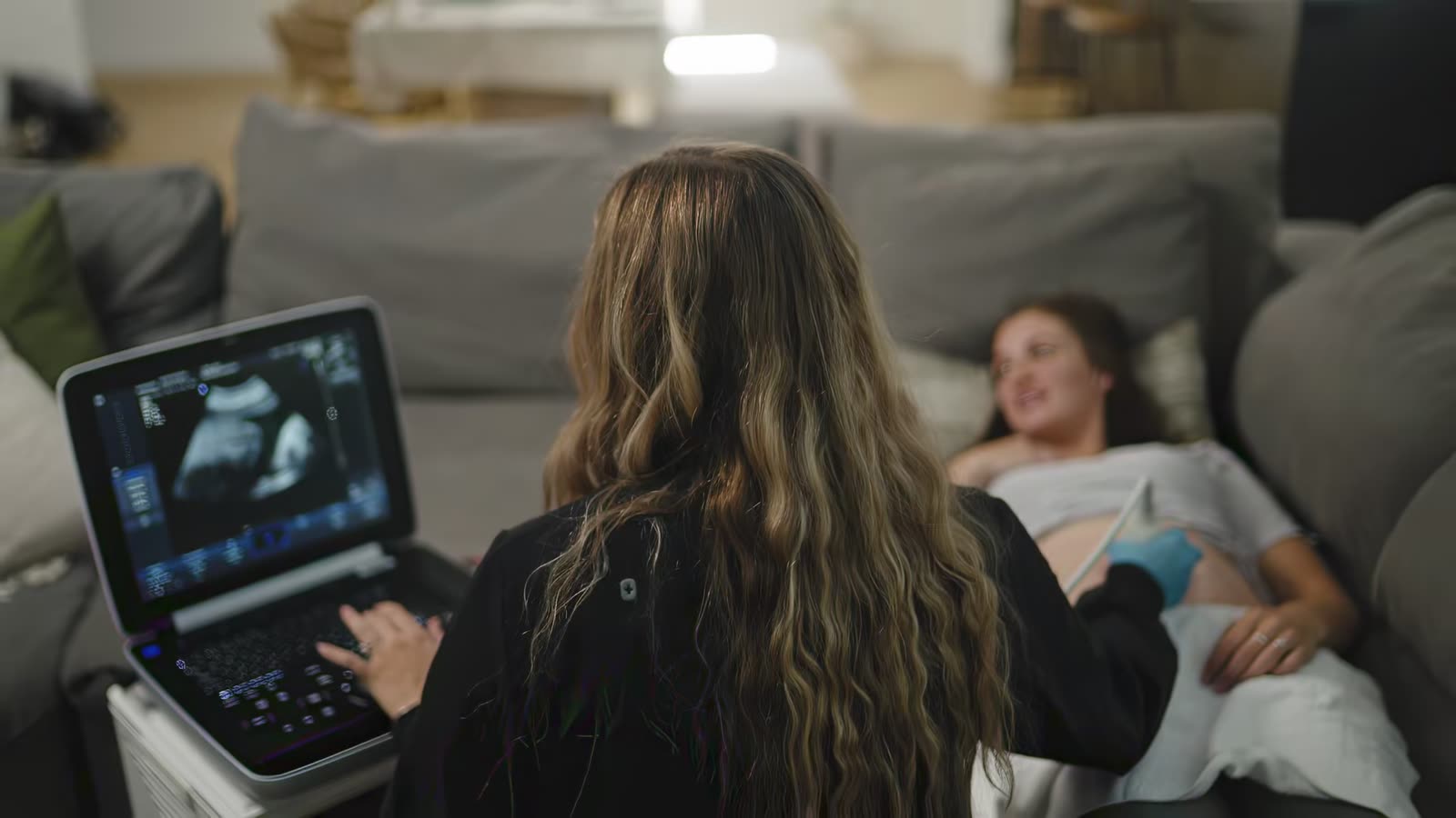 A Roam sonographer performing an ultrasound with a mom relaxing on her couch.